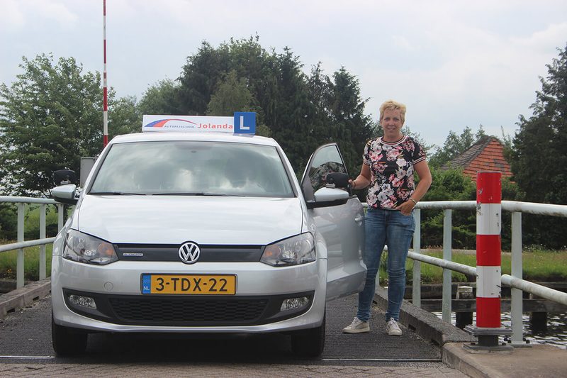 Jolanda naast haar lesauto met het L-bord en het daklicht van Autorijschool Jolanda